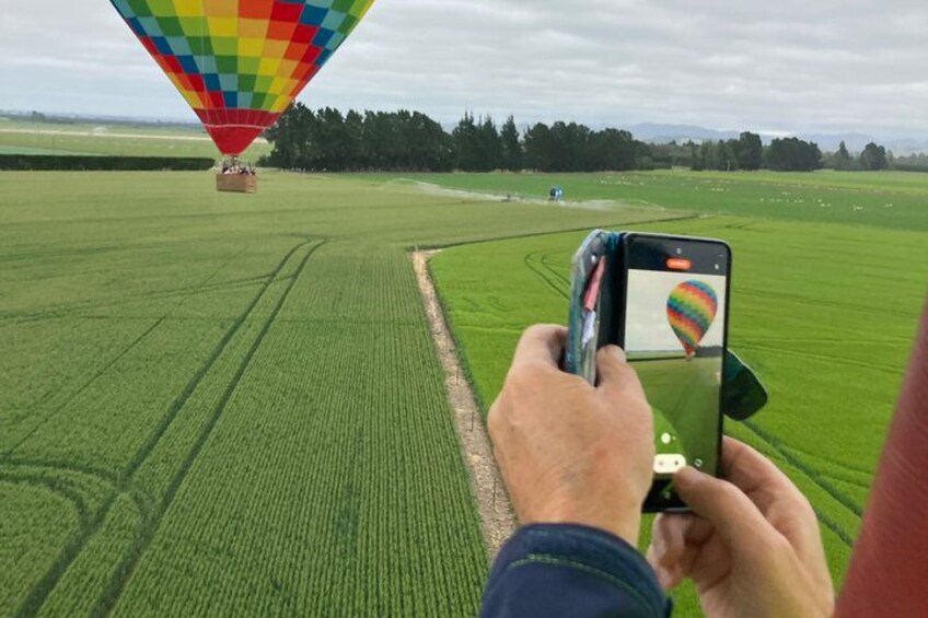A person holding a smartphone, taking a photo of a colorful hot air balloon in a green field. 3