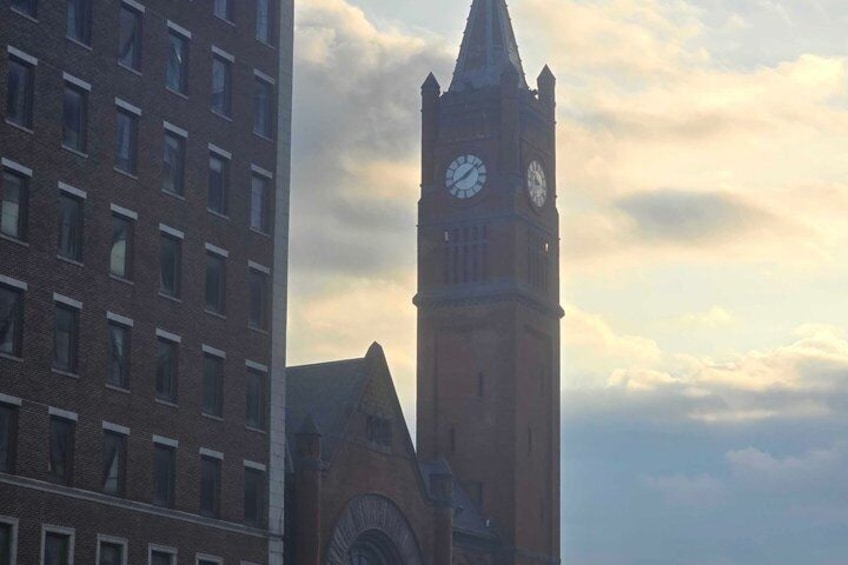 A clock tower with a pointed roof and a clock face, set against a cloudy sky. 3
