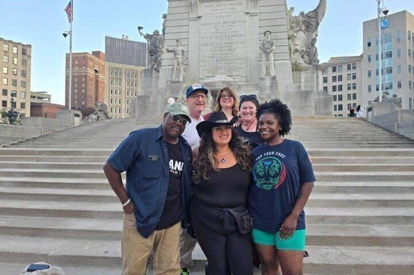 A group of people standing in front of a large monument with inscriptions and statues. 2