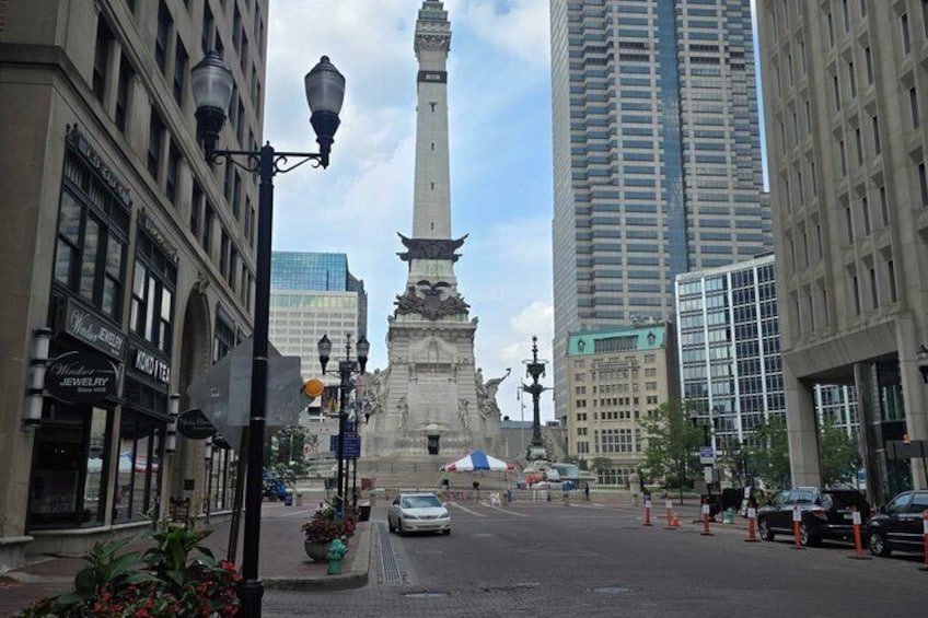 A street with a monument, buildings, and cars. 1