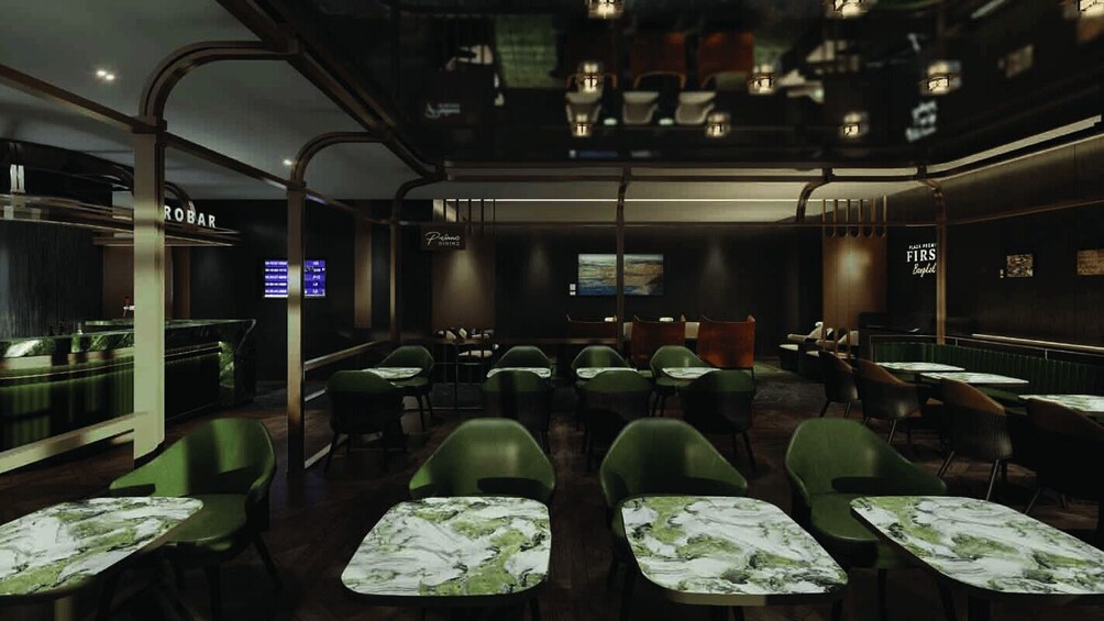A dimly lit restaurant interior with green chairs and tables, a bar area, and a digital menu display. 2
