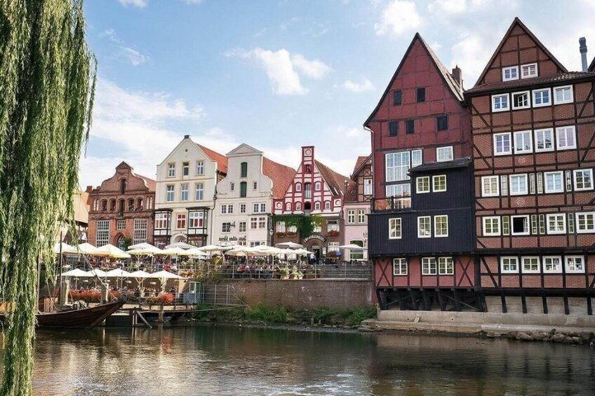 A riverside town with traditional half-timbered buildings, a bridge, and outdoor seating at a riverside café. 5