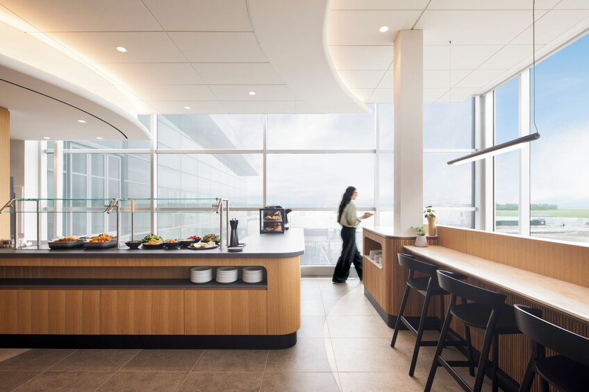 A modern cafeteria with a long counter, glass display cases, and a large window overlooking a cityscape. 2