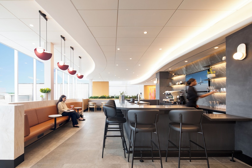 A modern bar with a counter, seating area, and a person working behind the bar. 1