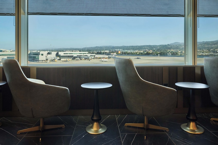 A modern interior with two chairs and a small table, a large window overlooking an airport and distant landscape. 2