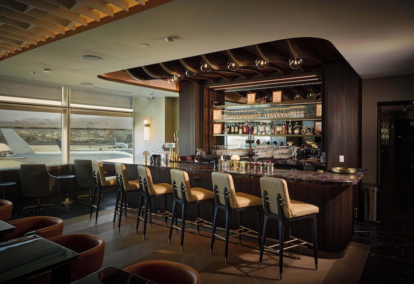 A bar with a curved counter, bar stools, and a view of an airport in the background. 4