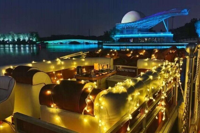 A boat with illuminated seating and a dining area, a bridge, and a dome structure in the background. 3