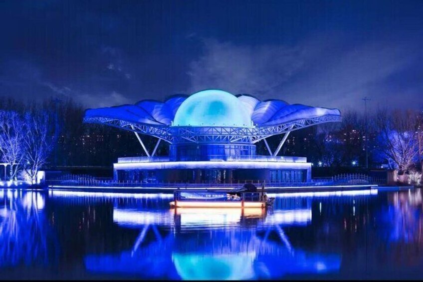 A large, illuminated structure with a dome-like roof reflecting on a body of water at night. 4