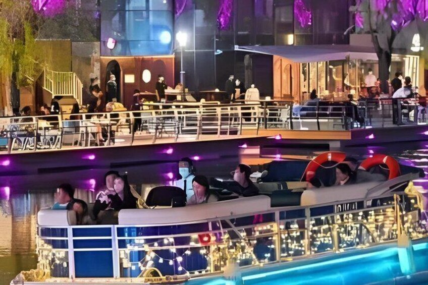 A boat with people on it, a dining area with tables and chairs, and a building with lights in the background. 5