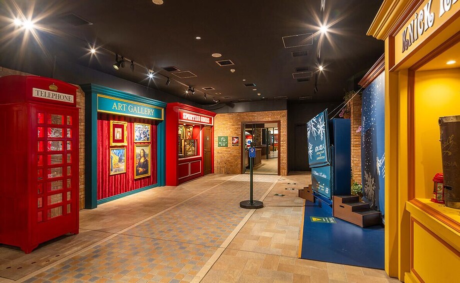 A museum corridor with red and blue themed exhibits, including a telephone booth and an art gallery. 1