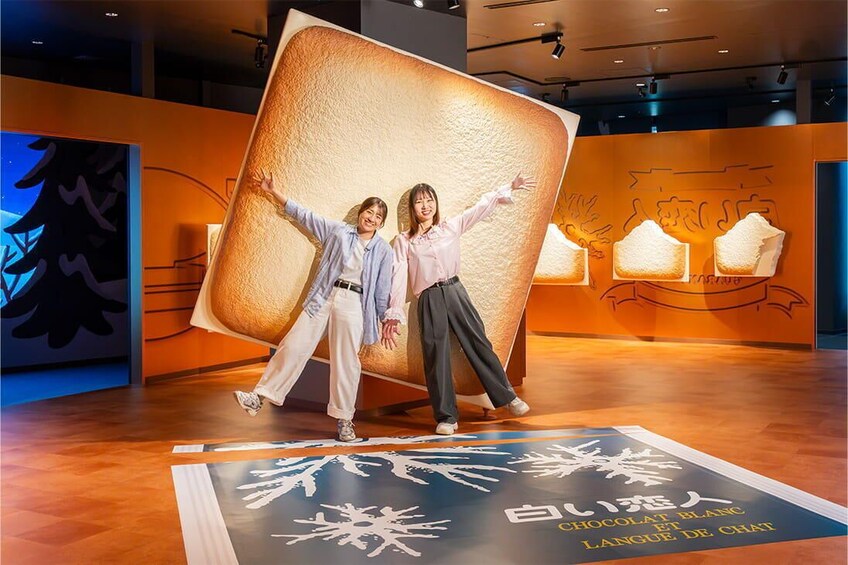 Two people posing in front of a large, textured sculpture resembling a loaf of bread. 3