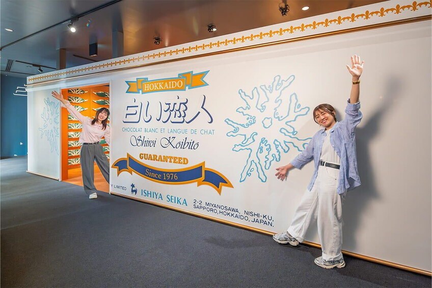A person standing in front of a wall with a large advertisement for Hokkaido chocolate. 2