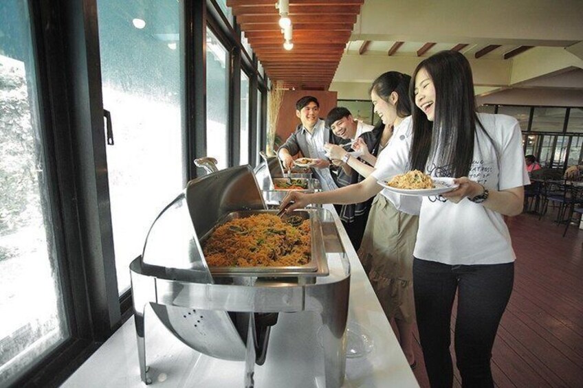 People serving themselves food at a buffet in a restaurant with large windows. 2