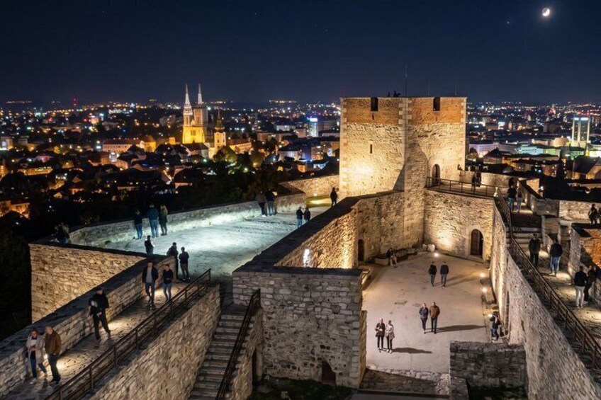 A historic stone fortress with battlements overlooking a cityscape at night. 5