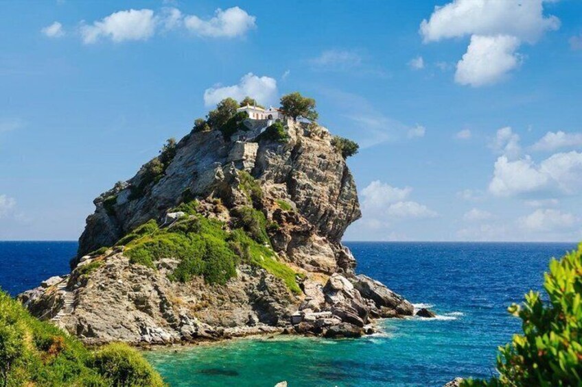 A rocky island with a building on top, surrounded by clear blue sea and sky. 1