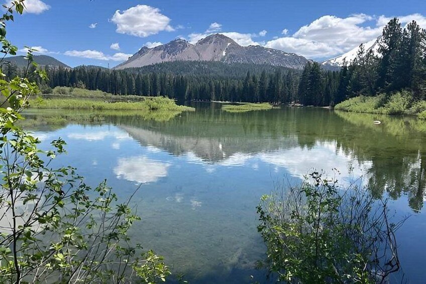 A calm lake with clear reflections, surrounded by dense forest and mountains under a blue sky. 3
