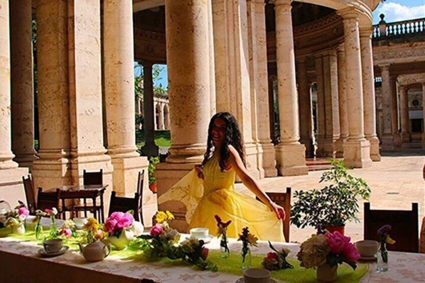 A woman in a yellow dress seated at a table with flowers and figurines. 4