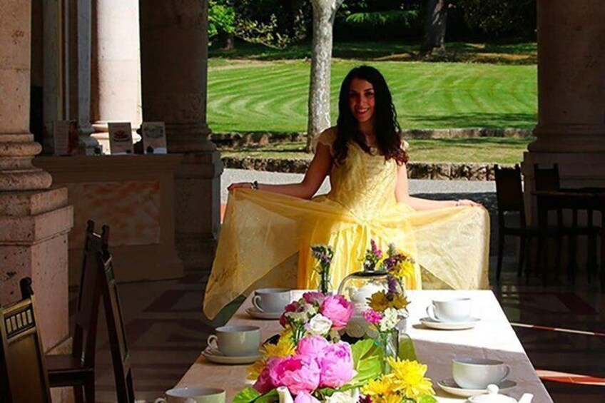 A person seated at an outdoor table with a yellow tablecloth, surrounded by flowers and a cup. 5