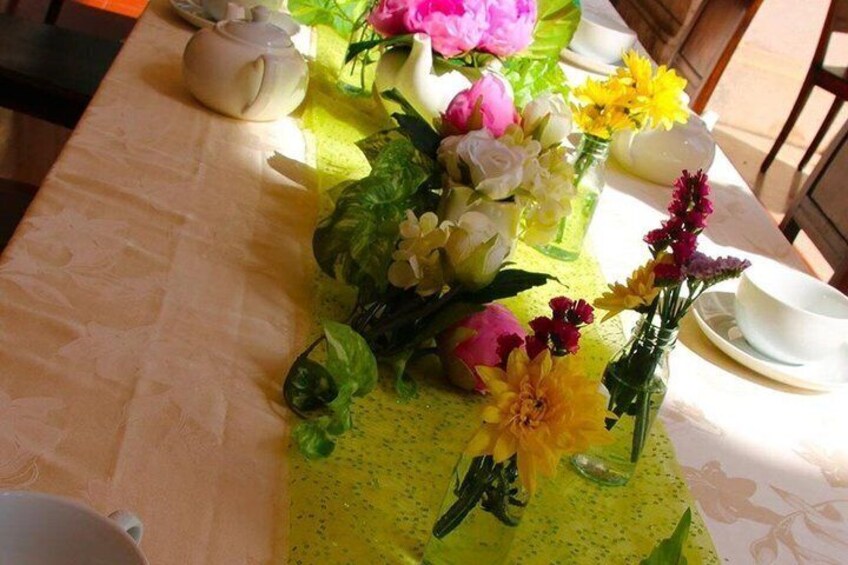 A table with a floral centerpiece, a teapot, and tea cups. 3