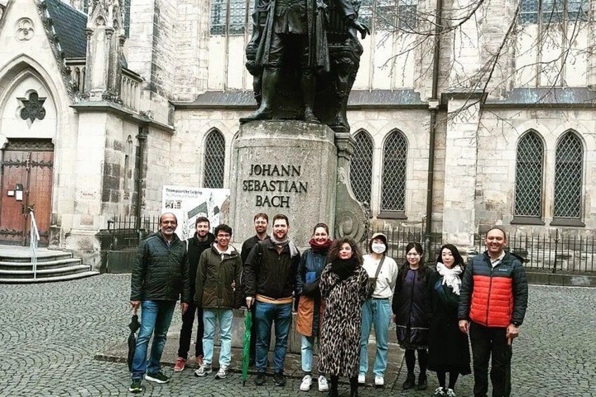 A group of people standing in front of a statue with a sign that reads 'JOHANN SEBASTIAN BACH'. 3