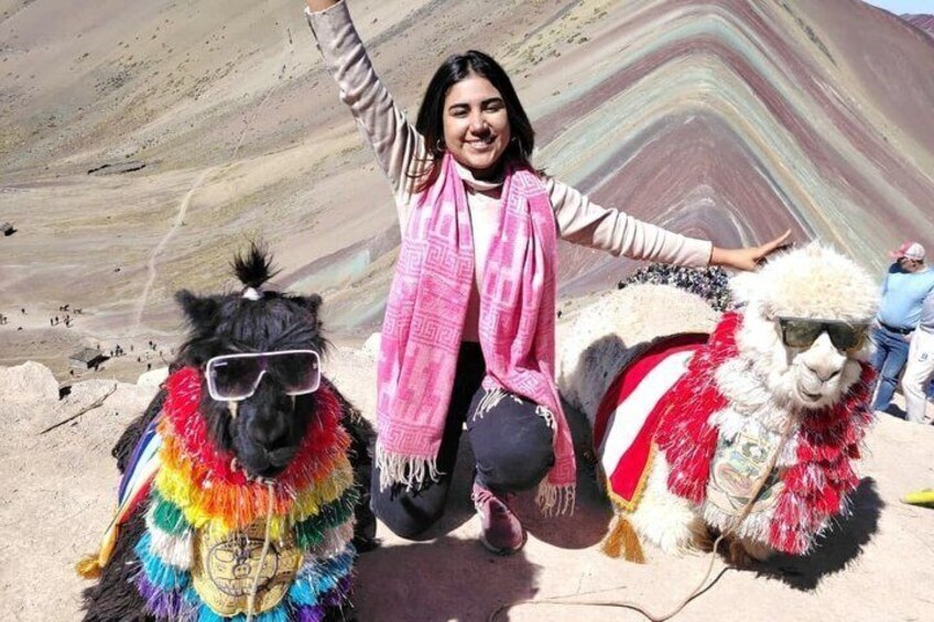 A person with a llama wearing sunglasses and a colorful outfit, standing in front of a mountain with layered rock formations. 5
