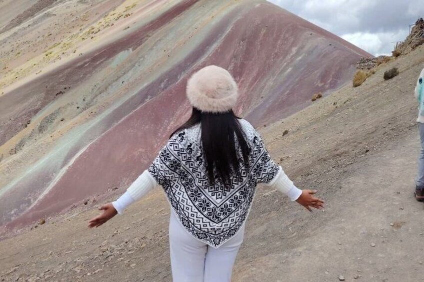 A person standing on a dirt path with arms outstretched, facing a large, multicolored rock formation. 3
