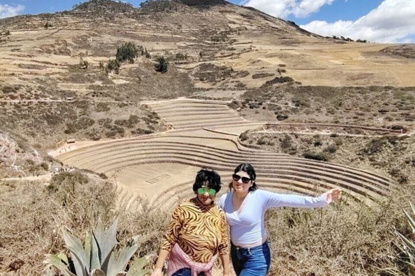 Two people standing in a dry, hilly landscape with terraced fields. 3