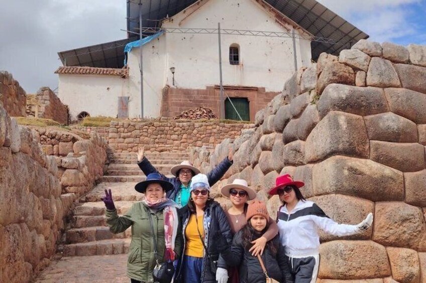 A group of people standing in front of a stone wall and a building with a sloped roof. 2