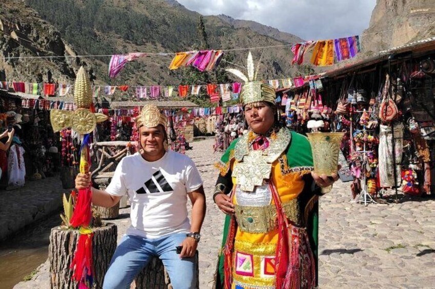 Two individuals in traditional attire, one holding a ceremonial staff, and a market stall with colorful textiles in the background. 1