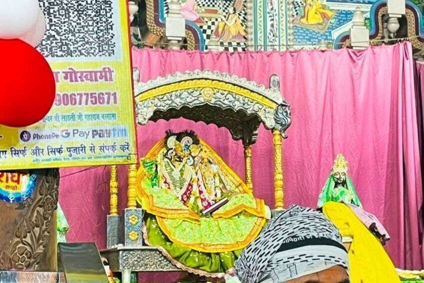 A traditional Indian shrine with a pink curtain backdrop, a decorated bed, and a statue of a deity. 5