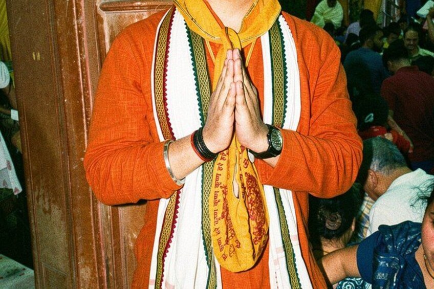 A person wearing an orange garment with a yellow scarf, standing with hands in a prayer position. 2