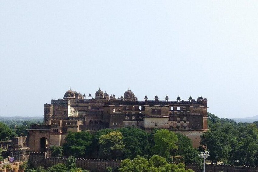 A large, historic building with multiple levels and domes, surrounded by lush greenery. 1