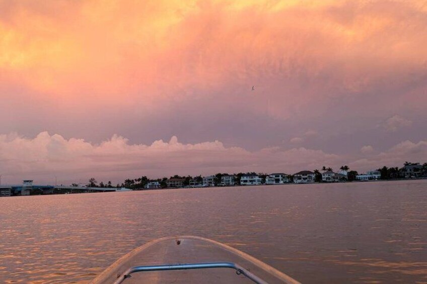 A boat on calm water with a sunset sky and a shoreline with buildings. 2