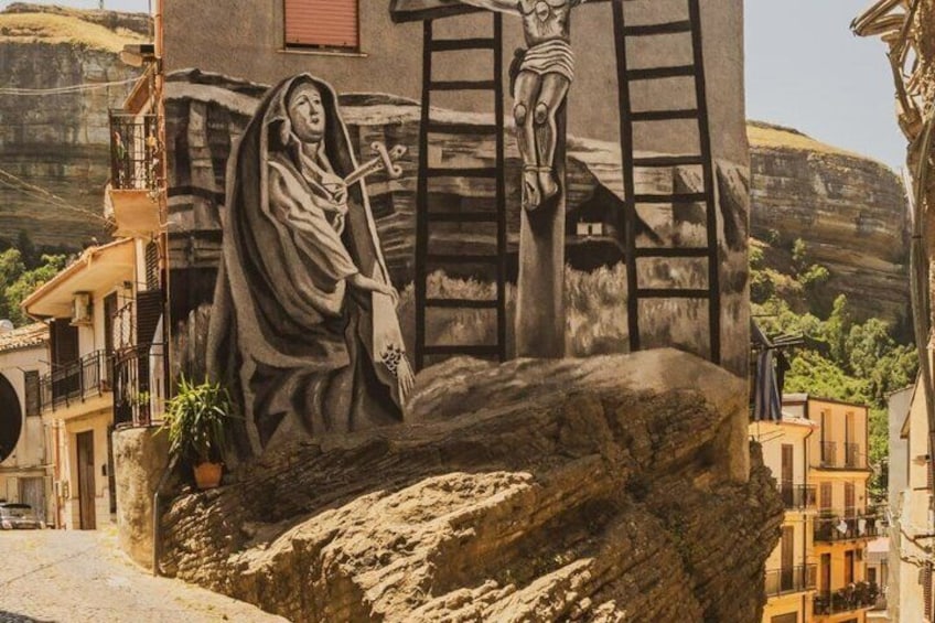 A mural of a woman holding a cross, a ladder, and a violin on a rock. 5