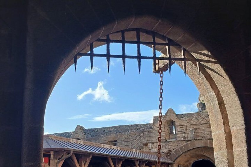 Una estructura de piedra en arco con una puerta metálica y cadena, que da vista a un edificio con techo de metal. 2