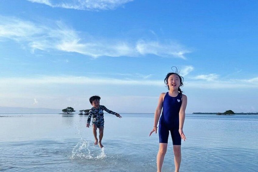 Two children playing in shallow water with a clear sky and distant land in the background. 3