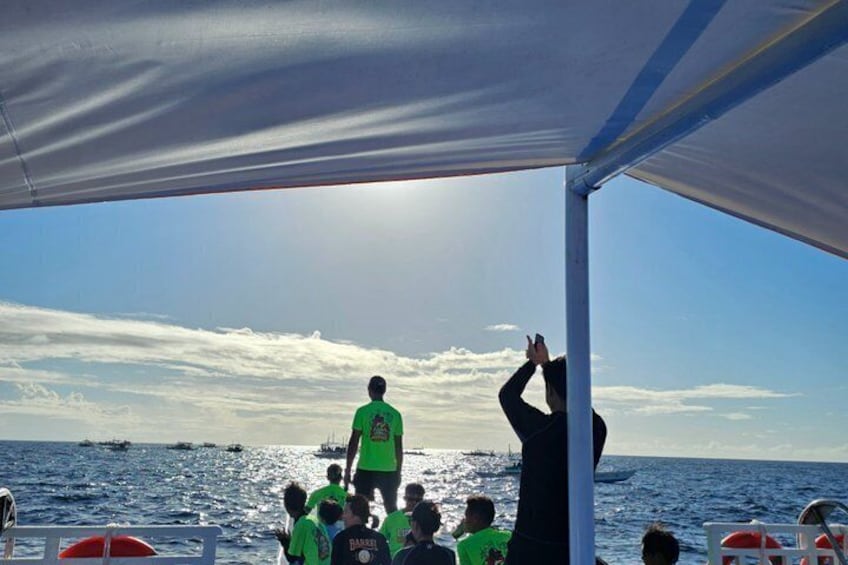 A boat with people on deck, a person in a green shirt standing on the bow, and the ocean in the background. 3