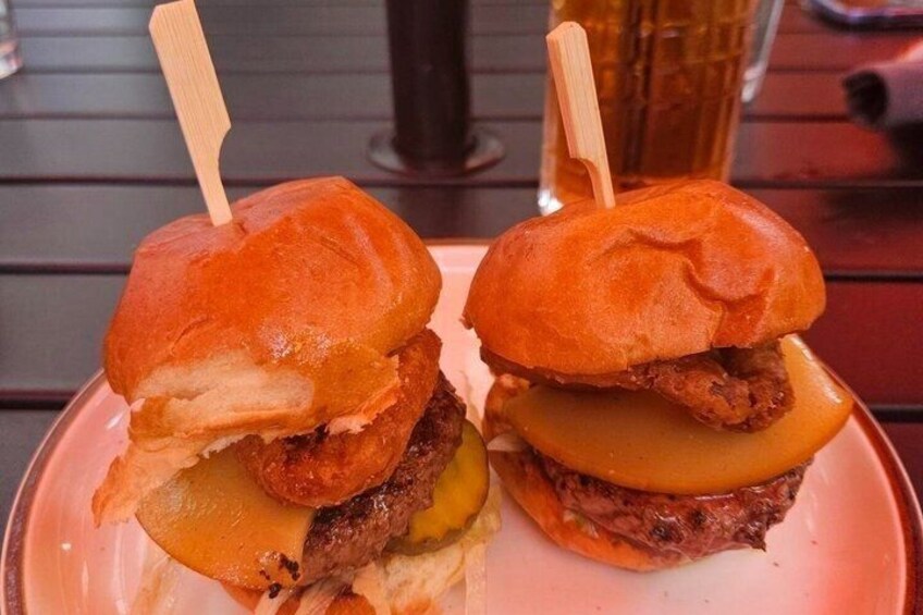 Two burgers with toothpicks, a glass of beer, and a red table. 2