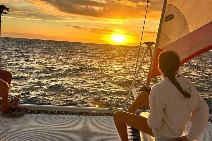 A sailboat at sunset with a person on deck and a woman looking out to sea. 5