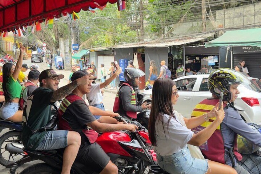 People on motorcycles, a white car, and a red car parked on a street with buildings and a sign that says 'HOTEL'. 2