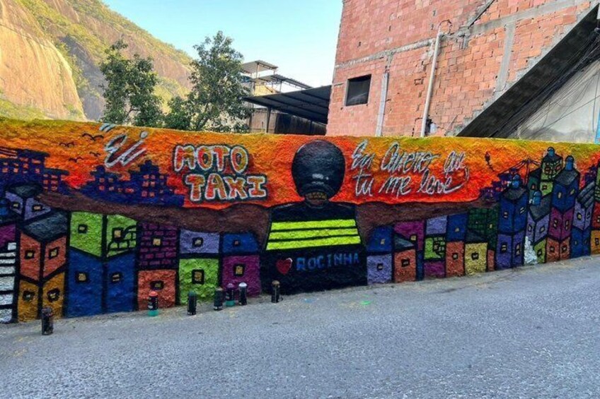 A colorful mural with a taxi service advertisement, a mountain in the background, and a building with a sloped roof. 3