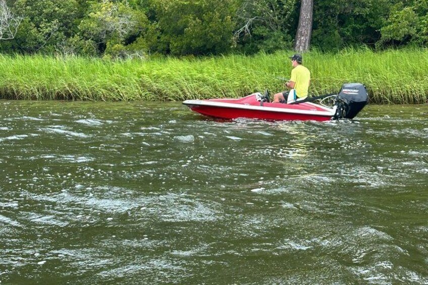A person in a yellow shirt on a red boat with an outboard motor on a river. 5