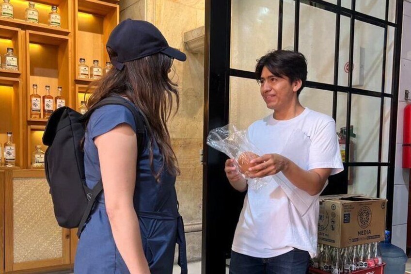 A person holding a wrapped item, another person with a backpack, and a shelf with bottles. 3
