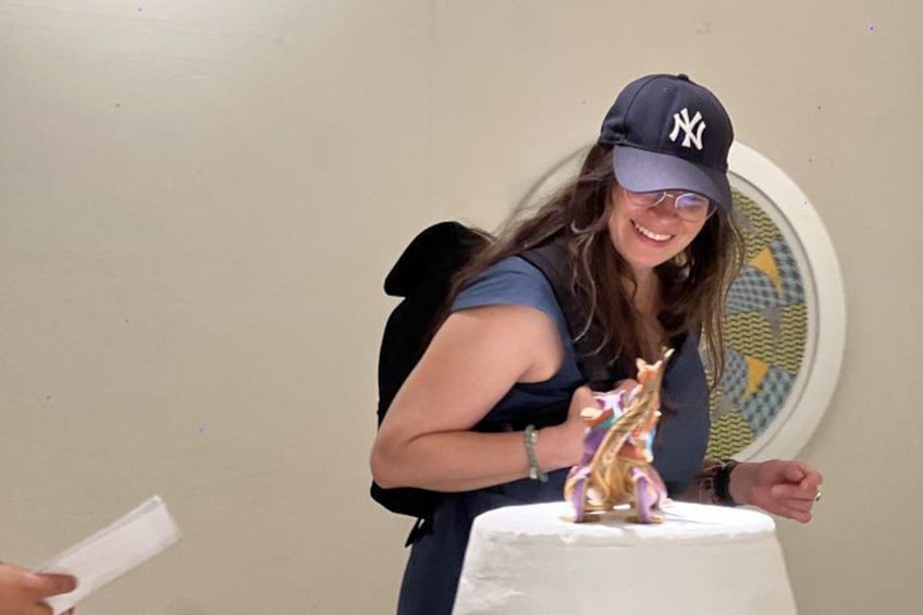 A person wearing a baseball cap and a sleeveless top, standing next to a white cake with a figurine on top. 5