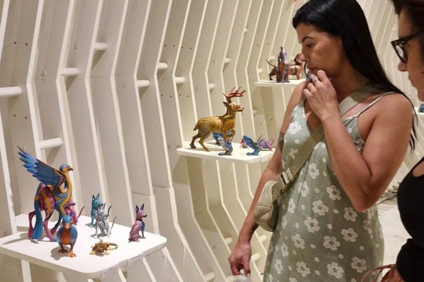 A person examining colorful figurines on a white shelf in a gallery. 2