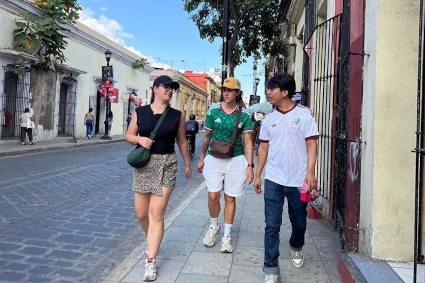 A street with people walking, buildings, and a tree. 1