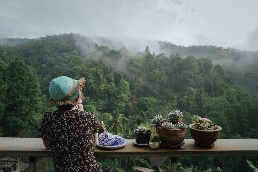 A person with a hat overlooking a forested area with potted plants on a balcony. 3