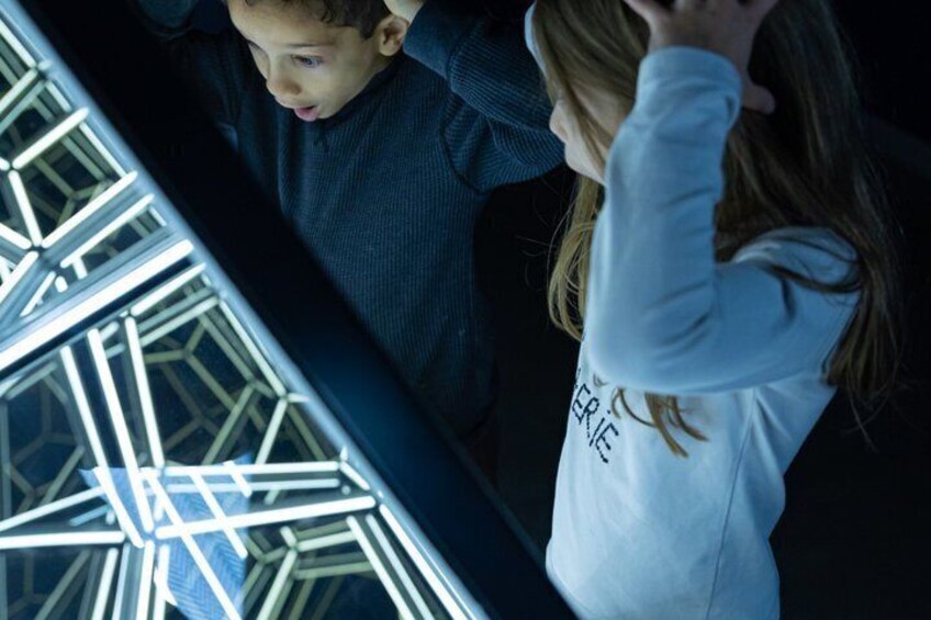 A person in a white hoodie with text, looking at a display of geometric shapes. 3
