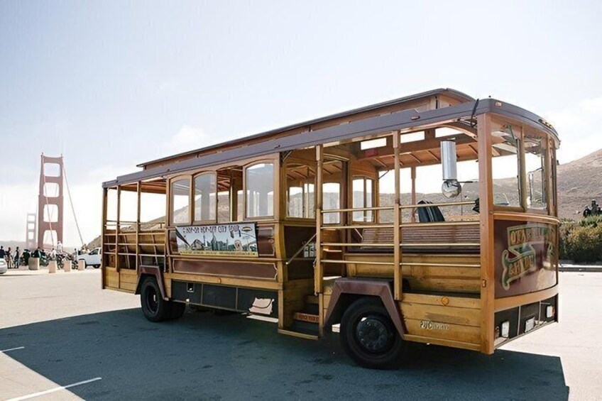 A vintage wooden bus parked on a street with a view of the Golden Gate Bridge in the background. 3