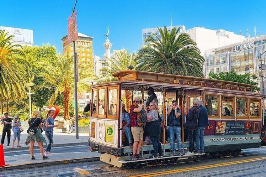 A cable car with passengers, palm trees, and buildings in the background. 1